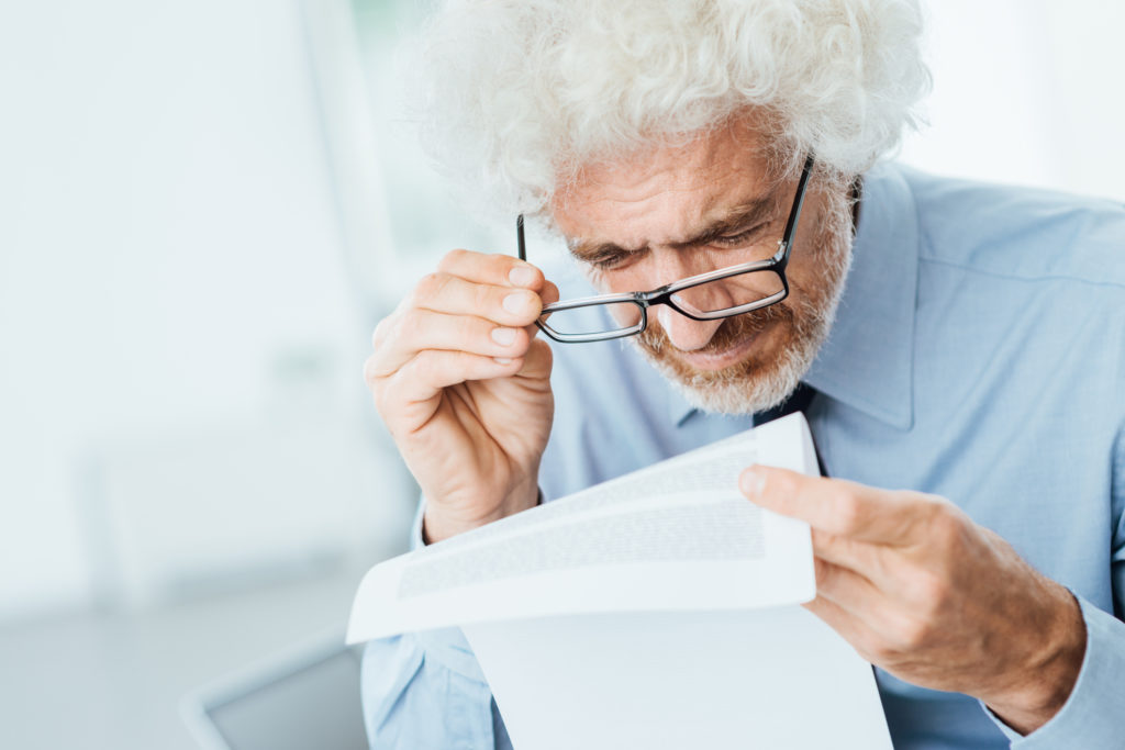 Mature male office worker having eyesight problems while reading paperwork with small text